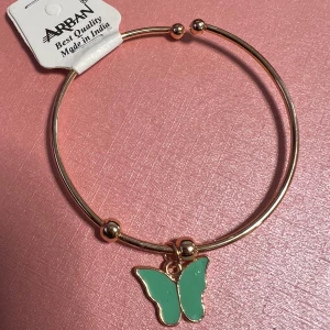 Guldarmband med grön fjärilsberlock barn storlek  - Elegant guldarmband från  med en charmig grön fjärilsberlock. Perfekt för att lägga till en färgglad touch till din stil. Tillverkat i Indien med hög kvalitet.