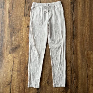 Beige/vita linnebyxor med snöre  - Säljer ett par beige/vita linnebyxor med elastisk midja och snöre. Säljer byxorna för att de inte kommer till användning längre.