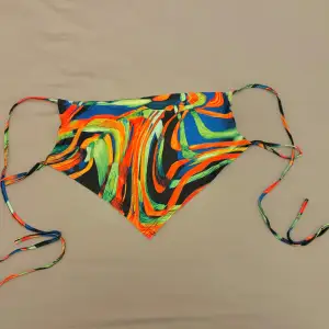 Säljer en färgglad topp med abstrakt mönster i blått, orange, grönt och svart. Bikinin har smala axelband och snörning i sidorna för justerbar passform. 🌸