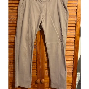 Beige chinos från Dressmann - Snygga beige chinos från Dressmann i slim fit. Byxorna har en klassisk design med knappar och dragkedja. Perfekta för en stilren look.