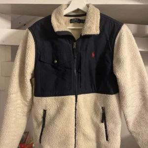 Fleecejacka från Polo Ralph Lauren - Säljer en snygg fleecejacka från Polo Ralph Lauren i beige och marinblått. Skick 9/10, nypris 3000kr mitt pris 1600kr. Skriv vid frågor!