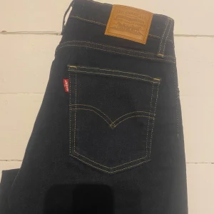 Levis jeans i mörkblå denim - Snygga Levis jeans i mörkblå denim med klassisk femficksdesign och gul kontrastsöm. De har en knappgylf och är högmidjade med en bootcut-stil. Perfekta för en stilren look. Knappt använda.