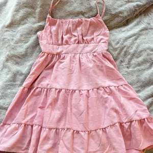 Rosa klänning med smala axelband - Söt rosa klänning med smala axelband som är justerbara. Klänningen har en smockdetalj på ryggen och ett diskret prickigt mönster. Perfekt för varma sommardagar!💞