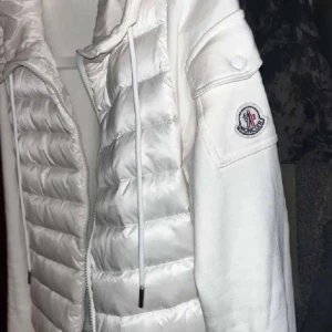 Vit dunjacka från Moncler - Snygg vit dunjacka från Moncler med pufferdesign och dragkedja. Jackan har långa ärmar och en hög krage för extra värme. Perfekt för kyliga dagar. För mer information kontakta mig 