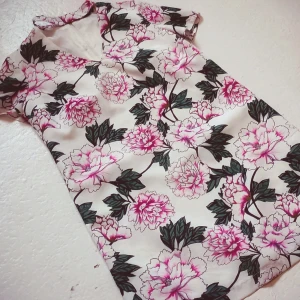 Blommig klänning från Mohito - Säljer en vacker blommig klänning från Mohito med rosa och gröna blommor på en vit bakgrund. Klänningen har korta ärmar och en dragkedja i ryggen för enkel påklädning. Perfekt för somriga dagar!