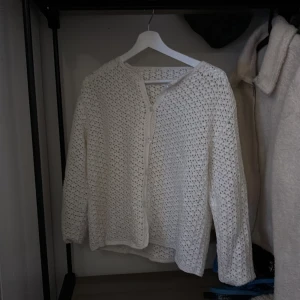 Vit stickad kofta - Säljer en söt vit stickad kofta med knappar framtill. Koftan har ett fint hålmönster och långa ärmar, perfekt för lager-på-lager-stil. Passar bra till både jeans och kjol!