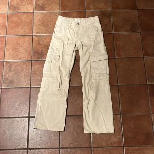 Beige cargobyxor från Gina Tricot - Snygga beige cargobyxor från Gina Tricot med flera praktiska fickor. Perfekta för en avslappnad stil. Byxorna har en rak passform och är tillverkade i ett bekvämt material.