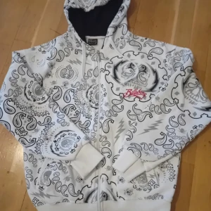 Vit hoodie med mönster från Billabong - Säljer en cool vit hoodie från Billabong med ett unikt svart och grått paisleymönster. Hoodien har dragkedja och en justerbar huva. Säljer för den inte passade! Skriv för frågor