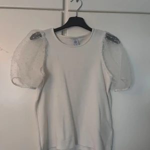 Vit topp med puffärmar - Säljer en söt vit topp från Lindex med unika puffärmar i transparent material med prickigt mönster. Perfekt för att ge en extra touch till din outfit. Storlek 146/152 men den passar bra på mig som är xs.
