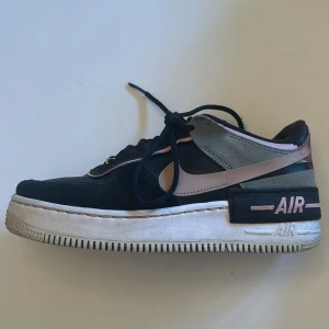 Nike Air Force 1 i svart och rosa - Snygga Nike Air Force 1 sneakers i svart med rosa och grå detaljer. Skorna har en klassisk design med snörning och en robust sula. Perfekta för en stilren look.