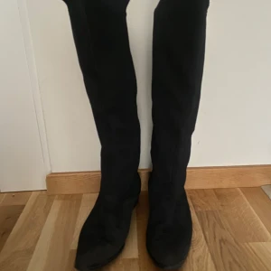 Svarta höga stövlar - Snygga svarta höga stövlar i mocka med en elegant design. Märke Petit Palmroth, Finland. Perfekta för att ge en stilren look till din outfit. De har en låg klack och en mjuk insida för extra komfort.  