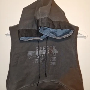 Grå ärmlös hoodie från Reebok - Säljer en grå ärmlös hoodie från Reebok med tryck på framsidan. Perfekt för en avslappnad stil eller träning. Stilen är lite tuff och sliten men som ni ser i nacken gällande storleken är den mint. Garderobsrensning så kika gärna på övriga auktioner.