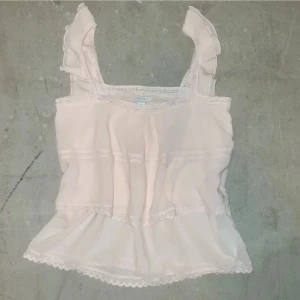 Puderrosa topp med spetsdetaljer från Amisu - Säljer en söt rosa topp från Amisu med spetsdetaljer och volanger på axelbanden. Toppen har en luftig passform och är perfekt för varma dagar. Den är tillverkad i ett lätt och bekvämt material. Finns fler bilder i min profil❗