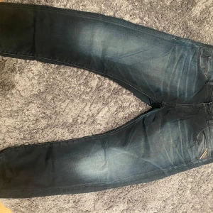 Mörkblå jeans från Replay - Snygga mörkblå jeans från Replay med en klassisk femficksdesign. Jeansen har en lätt tvättad look och orangea detaljer vid fickorna. Dessa jeans är även i bra skick då den endast använts ett fåtal gånger. Köpt för 1500kr.