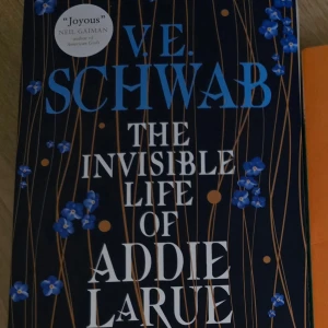 The Invisible Life of Addie LaRue - En fängslande roman av V.E. Schwab om Addie LaRue, en kvinna som gör en pakt för att leva för evigt men blir bortglömd av alla hon möter. Boken har en vacker omslagsdesign med blå blommor mot en mörk bakgrund.