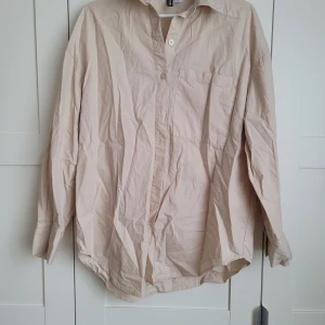 Beige skjorta från H&M Divided - Säljer en stilren beige skjorta från H&M Divided i storlek XS. Skjortan har långa ärmar och en klassisk krage med knappar framtill. Perfekt för en avslappnad men ändå snygg look.