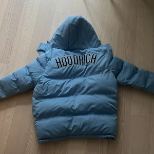 Blå pufferjacka från Hoodrich - Snygg blå pufferjacka från Hoodrich med huva och dragkedja. Jackan har långa ärmar och stora fickor framtill. Perfekt för kyliga dagar. Och jag har använt den typ 3 gånger