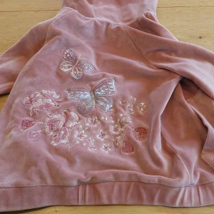 Rosa kofta med fjärilar - Söt rosa koftamed huva och dragkedja. Den har broderade fjärilar och blommor på ryggen och bröstet. Den är i barnstorlek!