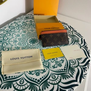 Mynt och Korthållare från - Hej! Jag säljer nu en ny samt oanvänd snygg korthållare i klassiskt monogrammönster med orange detaljer. Den har en dragkedja upptill och flera kortfack på framsidan. Perfekt för att hålla ordning på kort och kontanter. Alla tillbehör som finns med på bilderna medföljer självklart. Priset kan diskuteras vid snabb affär. Kan både frakta och mötas 