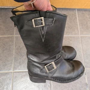 Johnny Bulls  - Snygga svarta stövlar i skinn med robusta spännen och dragkedja baktill. Perfekta för en tuff look och passar bra till höst- och vintergarderoben.