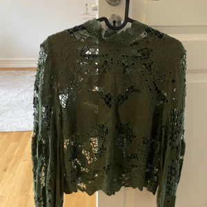 Olivgrön spetsblus - Säljer en elegant olivgrön spetsblus med intrikat mönster. Blusen har långa ärmar och en vacker design som passar perfekt för höst och vår. Perfekt för att ge en stilfull touch till din garderob.