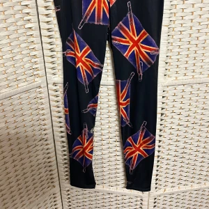 Svarta leggings med Union Jack-mönster - Coola svarta leggings med ett iögonfallande Union Jack-mönster. Perfekta för att sticka ut med en unik stil. De är stretchiga och bekväma, vilket gör dem idealiska för en avslappnad look.