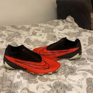 Röda fotbollsskor från Nike - Snygga röda fotbollsskor från Nike med svarta detaljer och en modern design. Skorna har en strömlinjeformad form och är perfekta för snabba rörelser på planen. Köptes för 1400kr och skorna har används ett par gånger men är fortfarande i perfekt form och har inga spår på skrapor eller hål:)