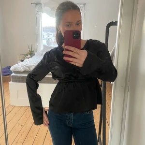 Svart satinblus - Snygg svart satinblus med v-ringning och långa ärmar. Blusen har en elegant passform med knytning i midjan som ger en smickrande siluett. Perfekt för både vardag och festliga tillfällen.❣️❣️
