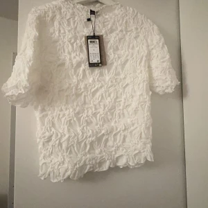 Vit blus med volangdetaljer - Säljer en vit blus från veromods med volangdetaljer över hela tyget. Blusen har korta ärmar och en luftig passform, perfekt för en stilren look. Ny med tagg kvar.