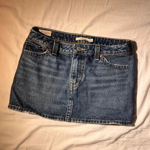 Jeanskjol från Levi's -  jeanskjol från Levi's i klassisk blå denim. Kjolen har en kort längd, sytt om sidan av kjolen hos en skräddare passar S-XS midjemått 72