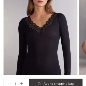 Svart långärmad topp med spetsdetaljer från intimissimi  - Elegant svart långärmad topp med v-ringad spetsdetalj. Perfekt för en stilren look.