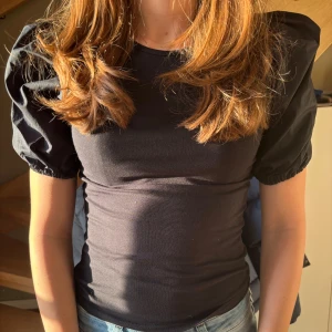 Svart topp med puffärmar - Snygg svart topp med puffiga kortärmar. Snygg och stilren. Toppen har en tight passform och är gjord i ett mjukt material. Helt oanvänd med prislappen kvar💕🕺