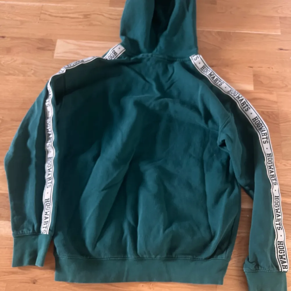 Säljer en grön hoodie med Harry potter -tryck och emblem på bröstet. Den har en stor ficka fram och text längs ärmarna. Perfekt för alla Harry Potter-fans! 🧙♂️Som ny och jätte finnt grön .. Neuletakit & Villapaidat.