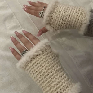 Virkade pärlvita handledsvärmare - Säljer ett par mysiga beige virkade  handledsvärmare med fluffiga kanter. Perfekta för att hålla händerna varma under kyliga dagar. De är handgjorda och har en mjuk och bekväm passform. Handtvättas. Nyskick då dem är helt nygjorda 😊