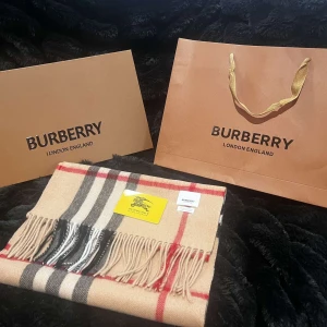 Beige rutig halsduk från Burberry - Säljer en elegant beige halsduk från Burberry med klassiskt rutigt mönster i svart, röd och vit. Halsduken har fransar i ändarna och är perfekt för att hålla dig varm och stilren under kyliga dagar.