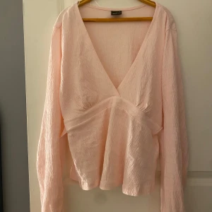 Ljusrosa blus från Gina Tricot - Säljer en söt ljusrosa blus från Gina Tricot med v-ringning och knytband i midjan. Blusen har långa ärmar och är tillverkad i ett lätt och luftigt material. Perfekt för en stilren look!
