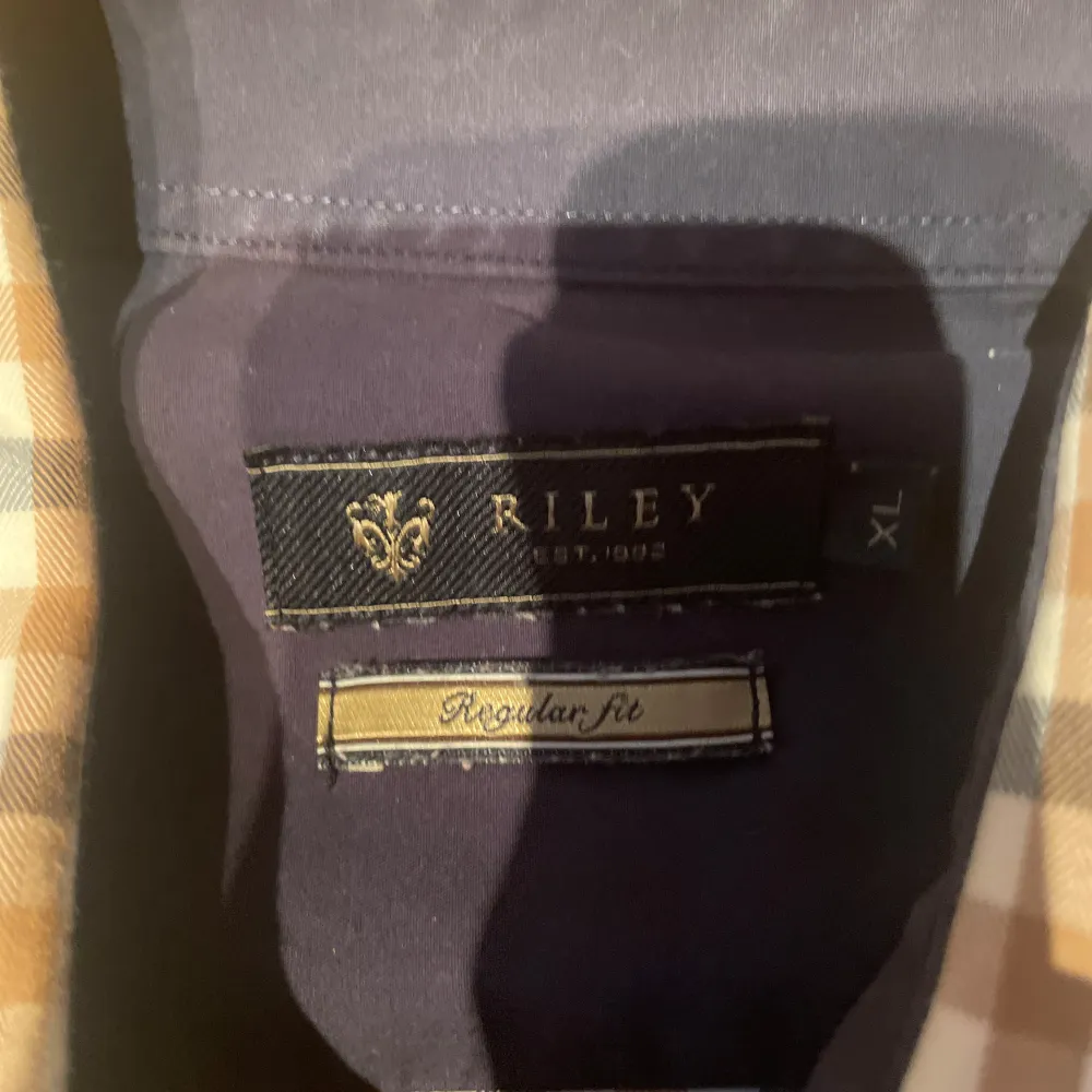 Snygg rutig skjorta från Riley i guldigt, svart och vitt. Skjortan har långa ärmar och stiliga armbågslappar i mörkare ton. Perfekt för en avslappnad men ändå uppklädd look.. Paidat.