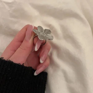 Silverfärgad blomring - En stilren ring i silverfärg med en stor blomma som dekoration. Perfekt för att ge en touch till din outfit. Använd 1 gång