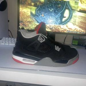 Svarta Nike Air Jordans med röda detaljer - Säljer ett par klassiska svarta Nike Air Jordans med röda och grå detaljer. Skorna har snörning och en ikonisk Nike Air-logga på hälen. Perfekta för sneakerheads som vill ha en tidlös stil.