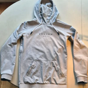 Ljusgrå vinterjacka från Dope - Säljer en ljusgrå vinterjacka från Dope med tryck både fram och bak. Den har en stor ficka framtill och justerbar huva med snören. Materialet är en blandning av nylon och spandex vilket gör den både bekväm och stretchig. Perfekt för kyliga dagar! ❄️