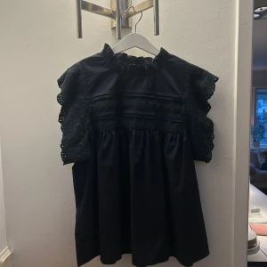 Mörkblå blus med spetsdetaljer!!!! - Säljer en snygg mörkblå blus med vackra spetsdetaljer på ärmarna. Blusen har en hög hals och volangdetaljer. Aldrig använd. Är osäker på märket då lappen inte är kvar