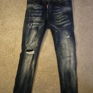 Mörkblå jeans med slitningar och färgstänk - Snygga mörkblå jeans från DS2 med coola slitningar och färgstänk. De har en straight passform och är perfekta för en avslappnad stil. Klassisk femficksdesign och knappgylf. Finns också kvitto.