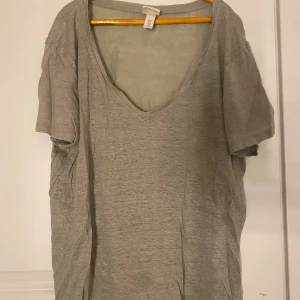 Grå t-shirt med v-ringning - En enkel och stilren grå t-shirt med v-ringning. Perfekt för en avslappnad look. T-shirten har korta ärmar och är tillverkad i ett mjukt material.