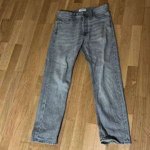 Grå jeans från Jack & Jones - Snygga grå jeans från Jack & Jones med klassisk femficksdesign. De har en lite mer baggy passform och är tillverkade i slitstarkt denim. Perfekta för en avslappnad stil.