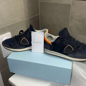 Philippe Model sneakers i svart blått och orange - Snygga sneakers från Philippe Model i en cool kombination av blått och orange. Skorna har en klassisk snörning och är tillverkade i skinn och mocka. Perfekta för en stilren look.