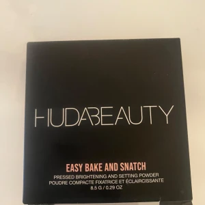 Easy Bake and Snatch Pressed Powder från Huda Beauty - Upptäck Huda Beauty's Easy Bake and Snatch, ett pressat puder för ljusare och fixerande finish. Perfekt för att sätta sminket och ge en jämn hudton. Kommer i en stilren förpackning med spegel. Färgen är cherry blossom cake. Oanvänd 