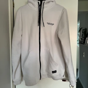 Vit hoodie från Race Marine - Säljer en stilren vit hoodie från Race Marine. Den har en dragkedja framtill och en justerbar huva med svarta snören. Perfekt för en avslappnad stil. Två praktiska fickor framtill.