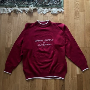 Röd tröja från Peak Performance - Säljer en snygg röd tröja från Peak Performance med texten 'Marine Supply' på bröstet. Tröjan har vita detaljer vid hals, ärmslut och nederkant. Perfekt för en stilren look.