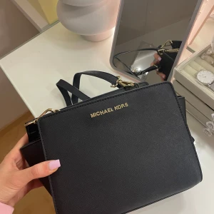 Svart axelväska från Michael Kors - Snygg svart axelväska från Michael Kors med guldfärgade detaljer och dragkedja. Väskan har en justerbar axelrem. Rymlig insida med ett fack. Knappt använd.