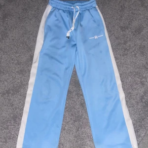Byxor från Amiri - Snygga ljusblå byxor från Amiri med vita sidopaneler. Byxorna har elastisk midja med snörning och en bakficka. Perfekta för en avslappnad och clean stil. Passar väldigt bra om man är 170-180cm lång. Kan fraktas och även hämtas upp i Gävle. Priset är inte hugget i sten, kan gå ner vid snabb affär 